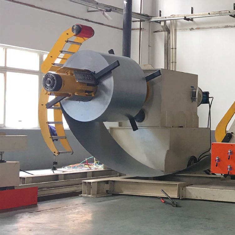 Desbobinador hidráulico con bobina cargada y brazo presor superior en un entorno industrial