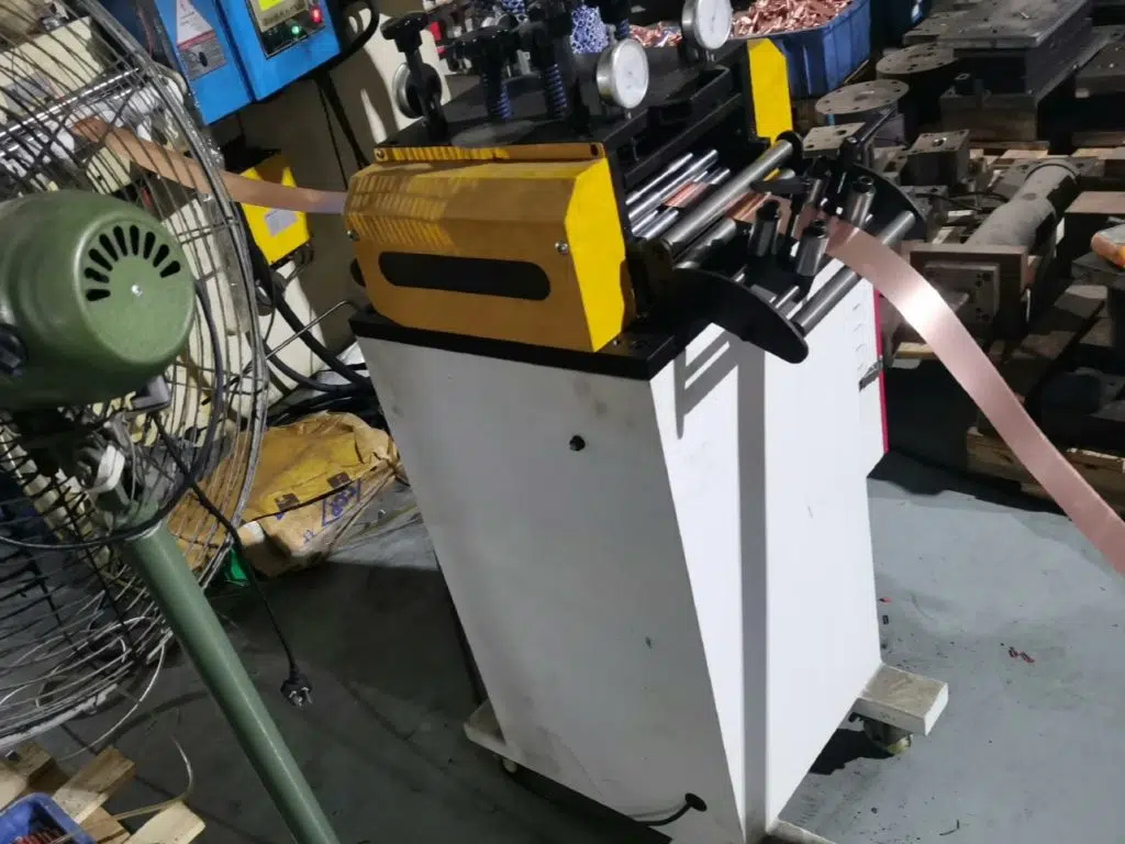 Niveladora compacta amarilla procesando una tira metálica de color cobre